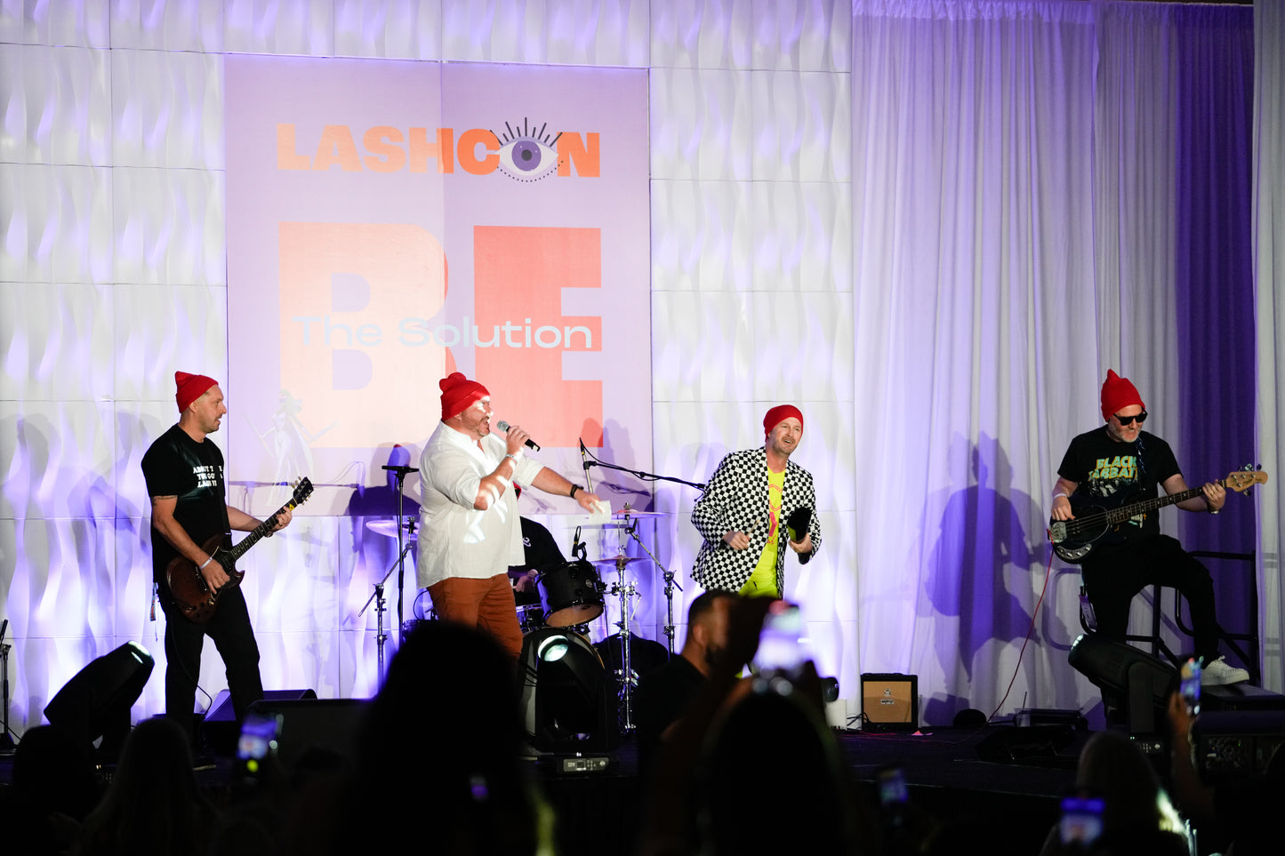 Band performing on stage with bright purple lighting and LASHCON VIP logo projected in the background.